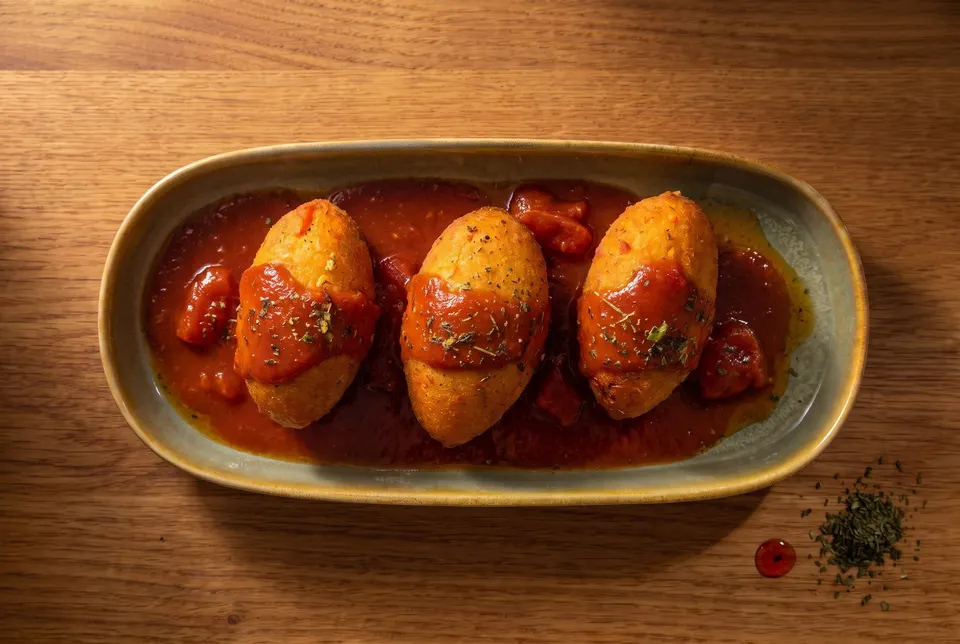 Three kutlik, stuffed bulgur dumplings, in tomato sauce on an oval platter (illustrative image)