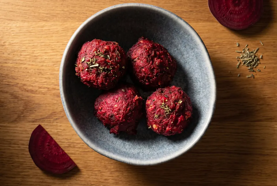 Bowl of dark red beetroot falafel, with a slice of beetroot beside it (illustrative image)