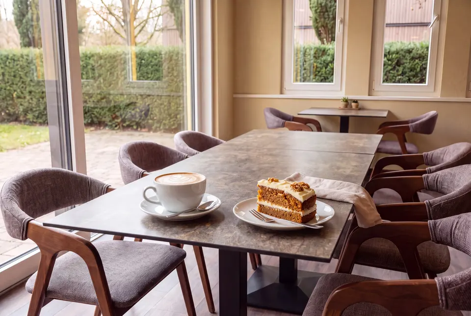 Cappuccino und ein Stück Rüeblikuchen auf dem Tisch am Fenster des Lokals (Symbolbild)