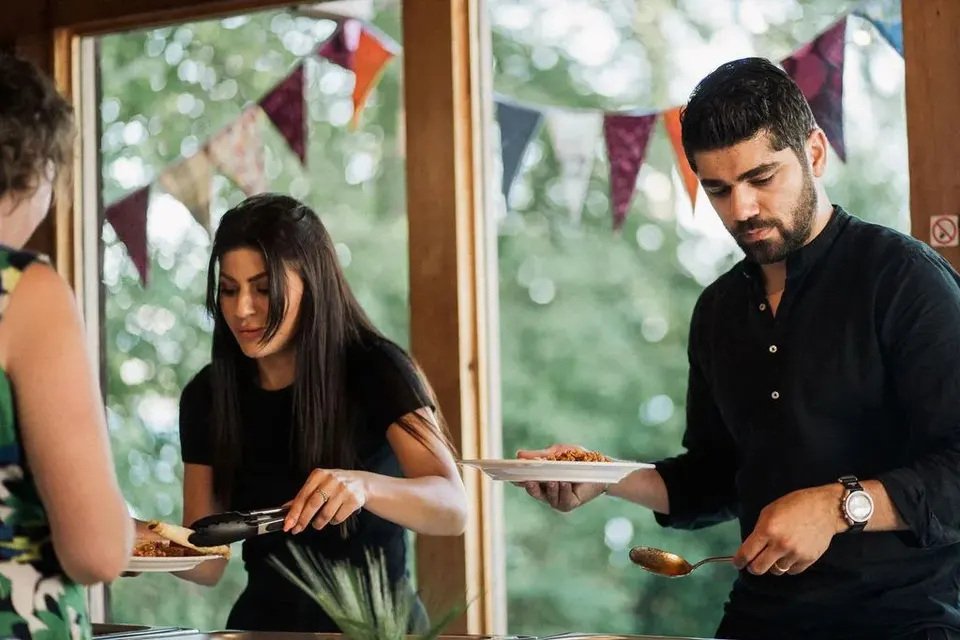 Zwei Gäste schöpfen sich am Catering-Buffet in einem Raum mit Fahnengirlanden