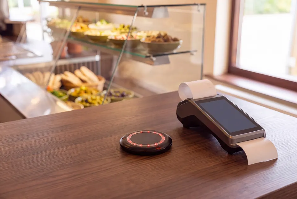 Black restaurant pager with a red light ring on the counter next to the card terminal (illustrative image based on a photograph of the premises)